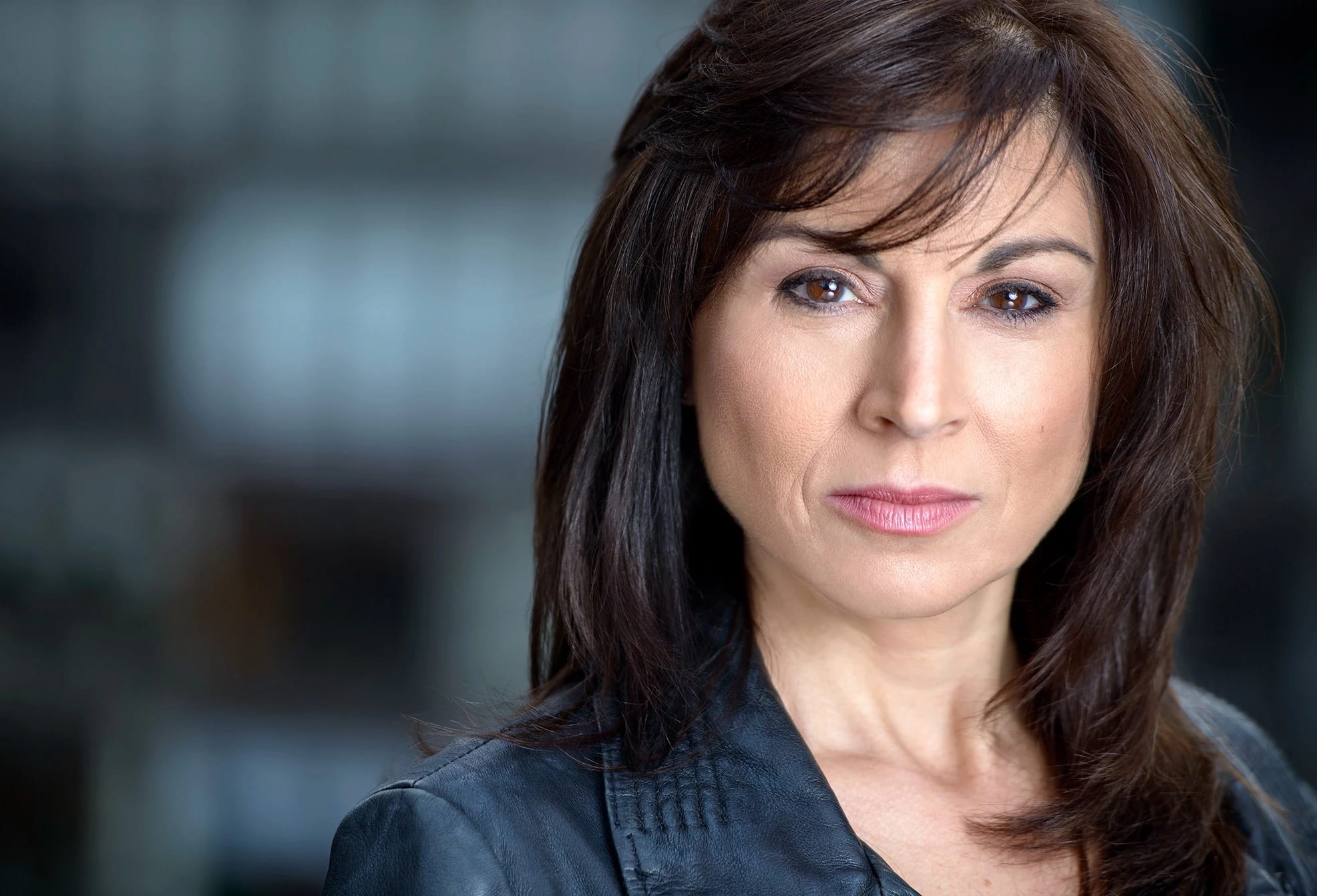 A headshot of a middle aged woman with long brown hair wearing a black jacket.