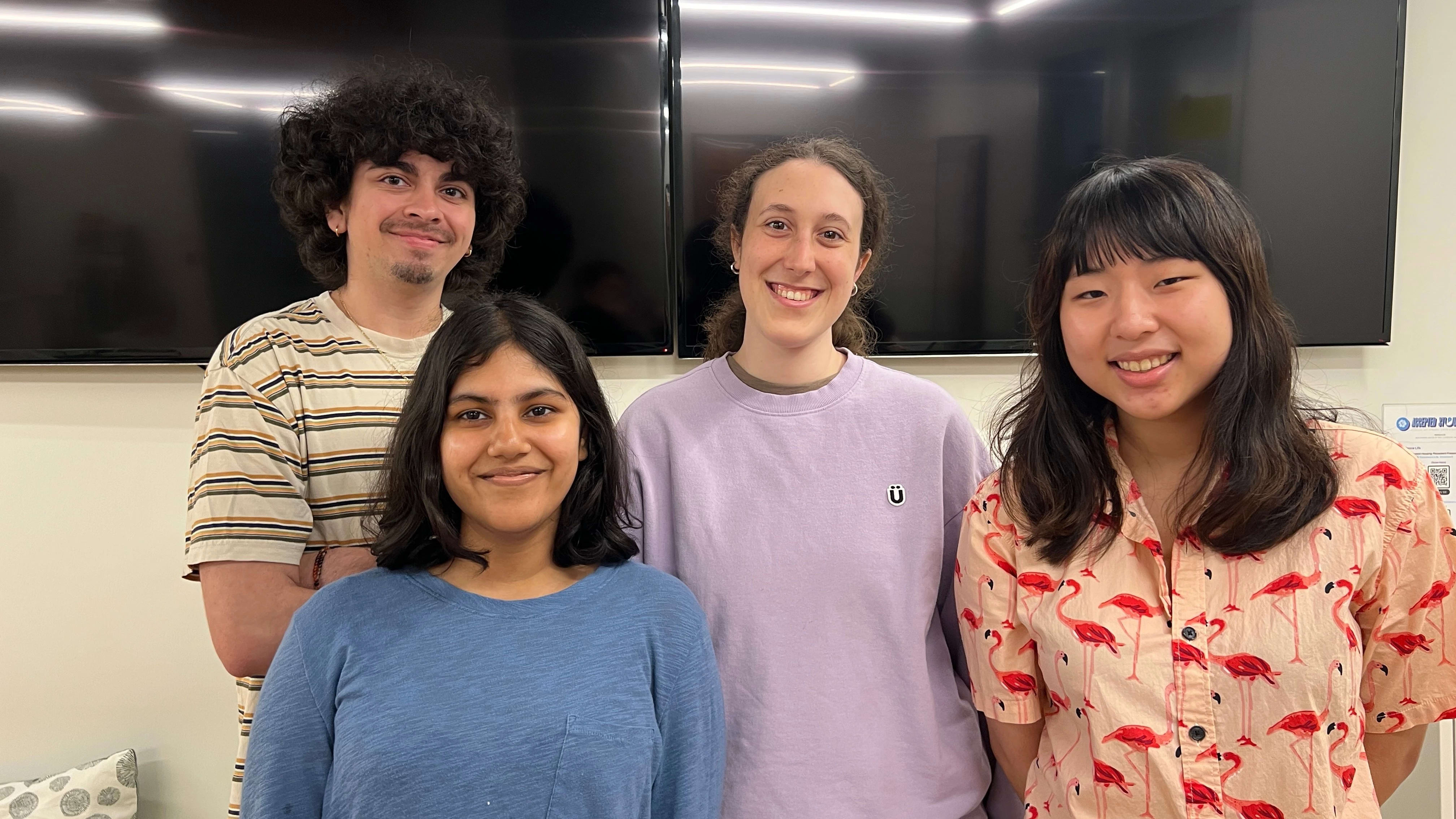 Four VASA officers standing in front of white wall with two mounted tv screens.