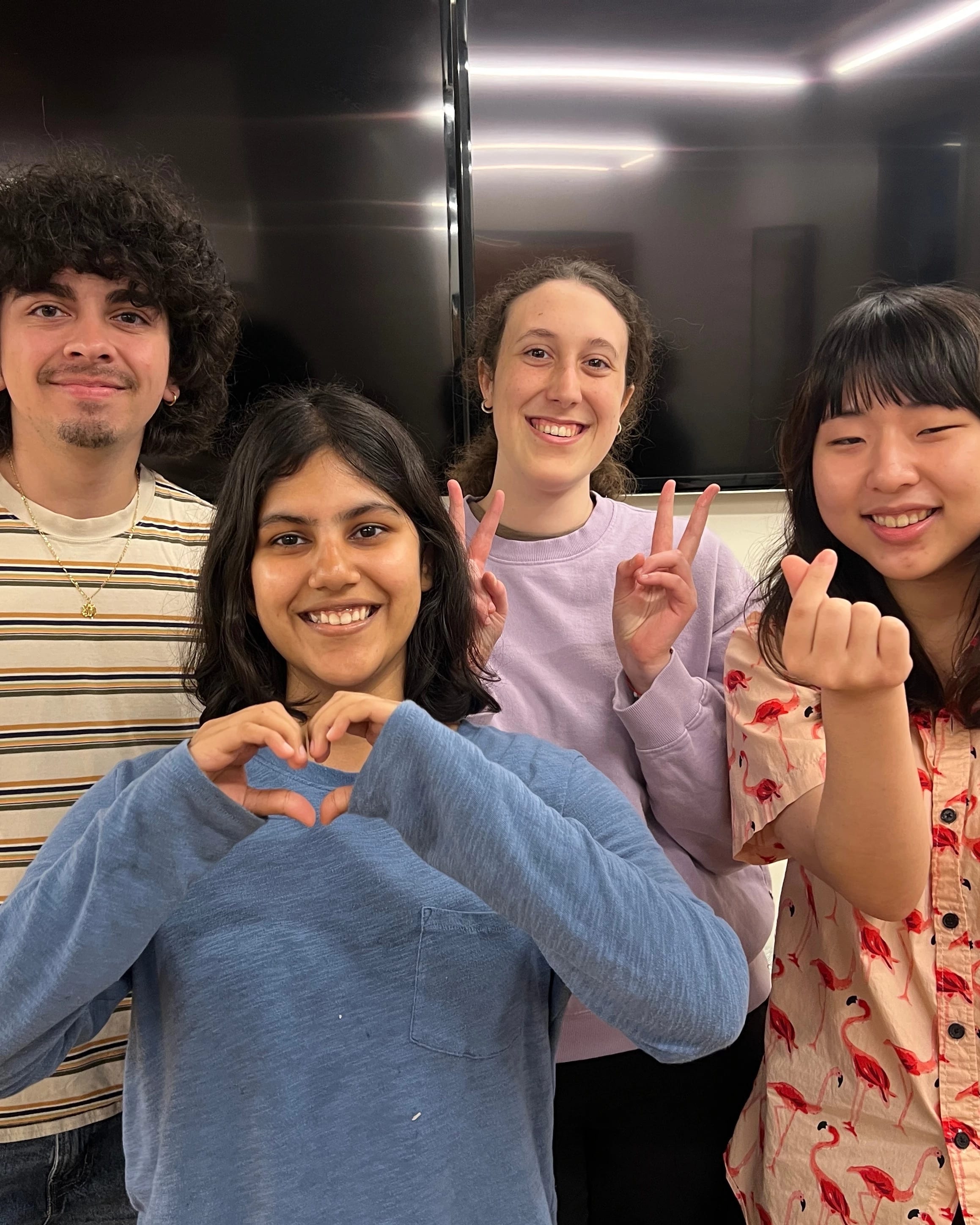 Four VASA officers standing in front of white wall with two mounted tv screens. The officers are giving peace and heart signs with their hands.