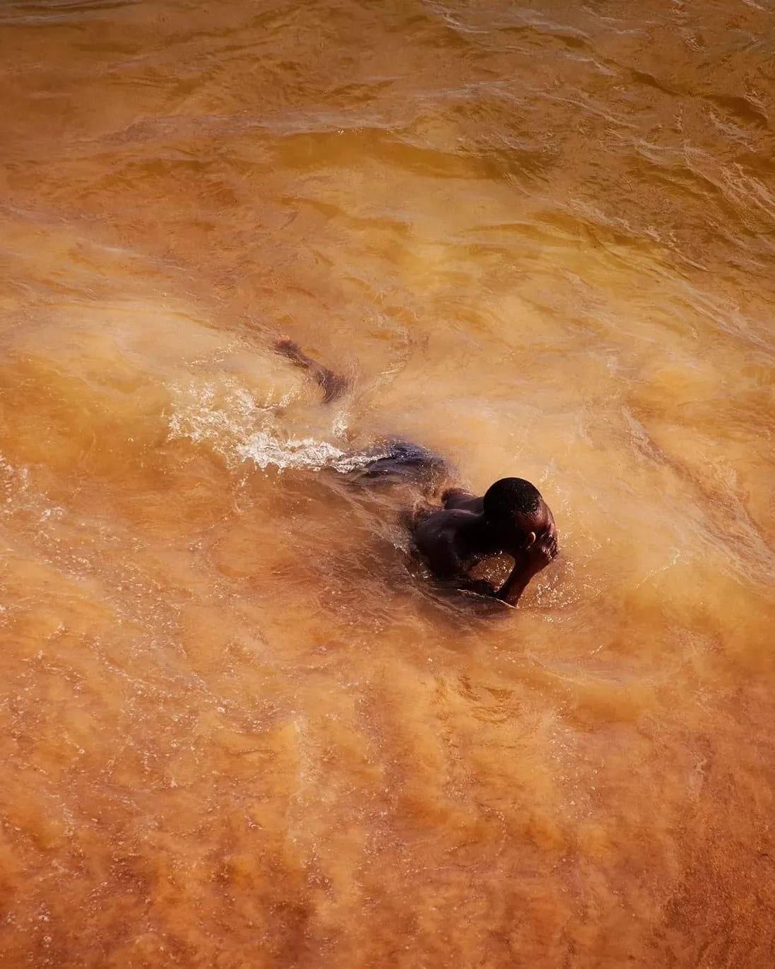 In this color photograph, a man emerges from the ocean, which has taken on a vibrant orange-ish cast in rural Saly, Senegal.