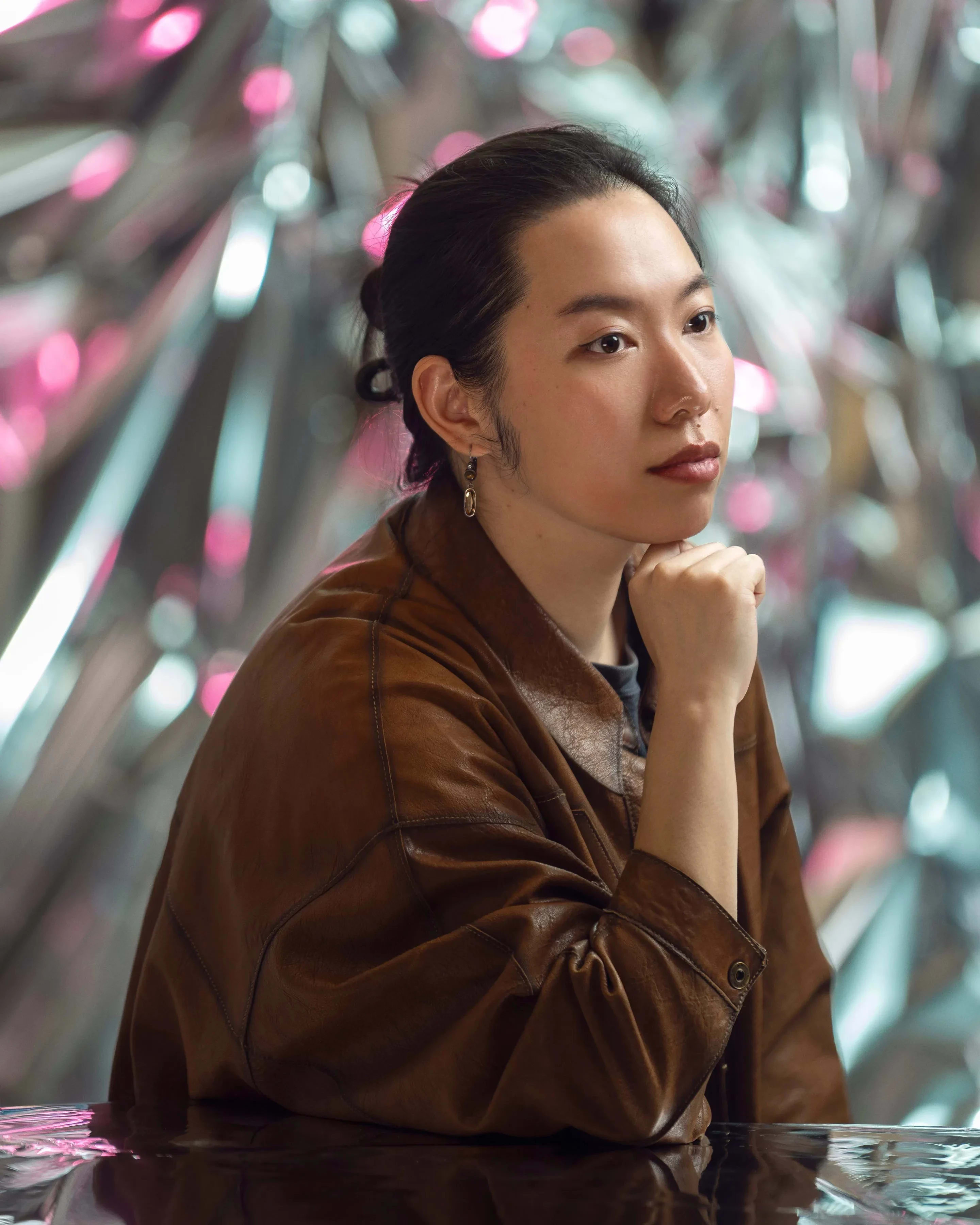 A person rests their chin on their fist as they look off to the side in front of a reflective background.