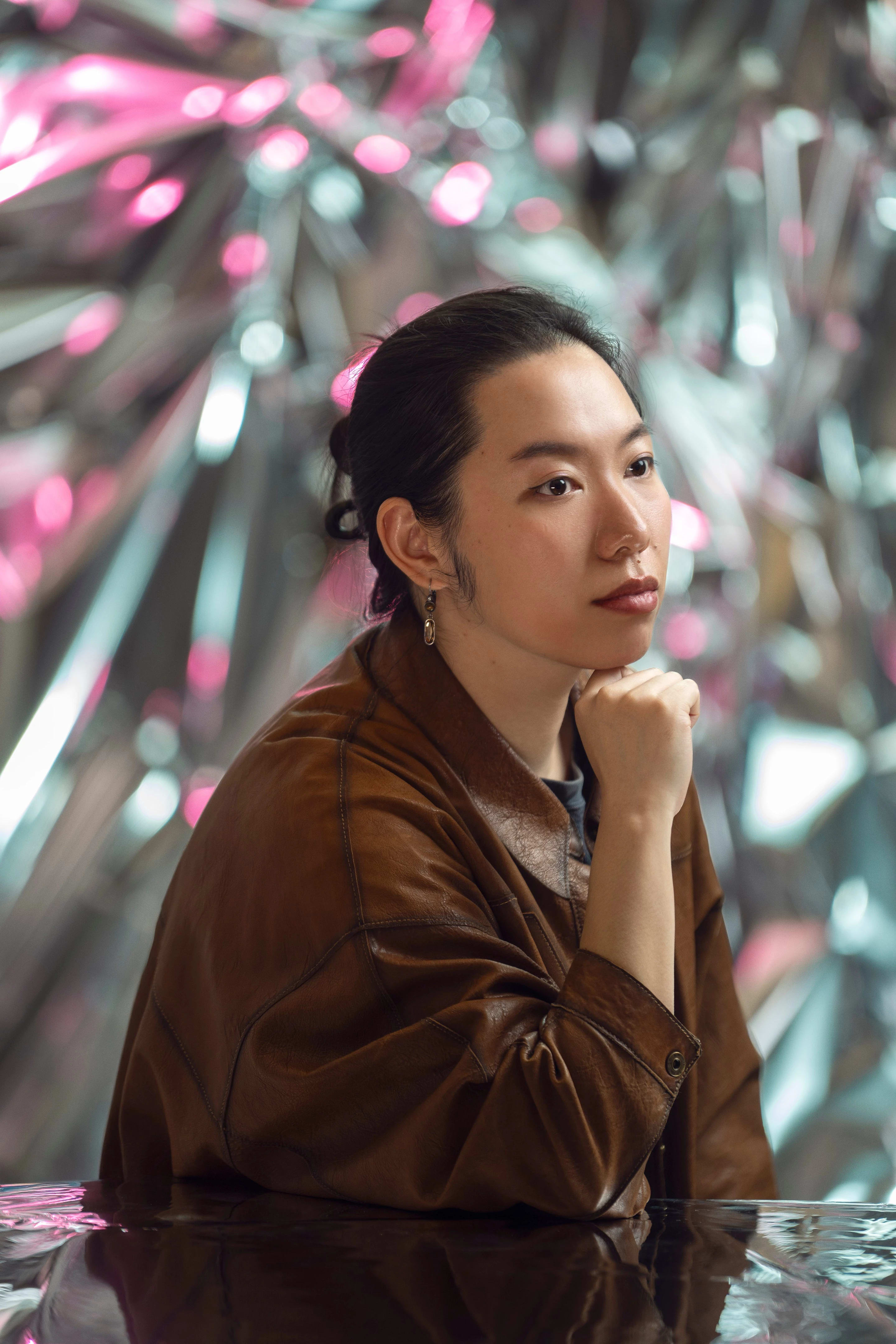 A person rests their chin on their fist as they look off to the side in front of a reflective background.