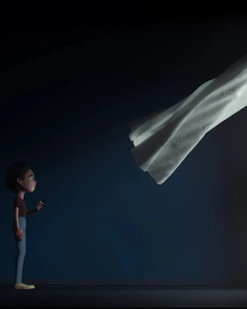 A student stands in a dark empty room with a window. They're looking out the window while the curtain billows into the room.