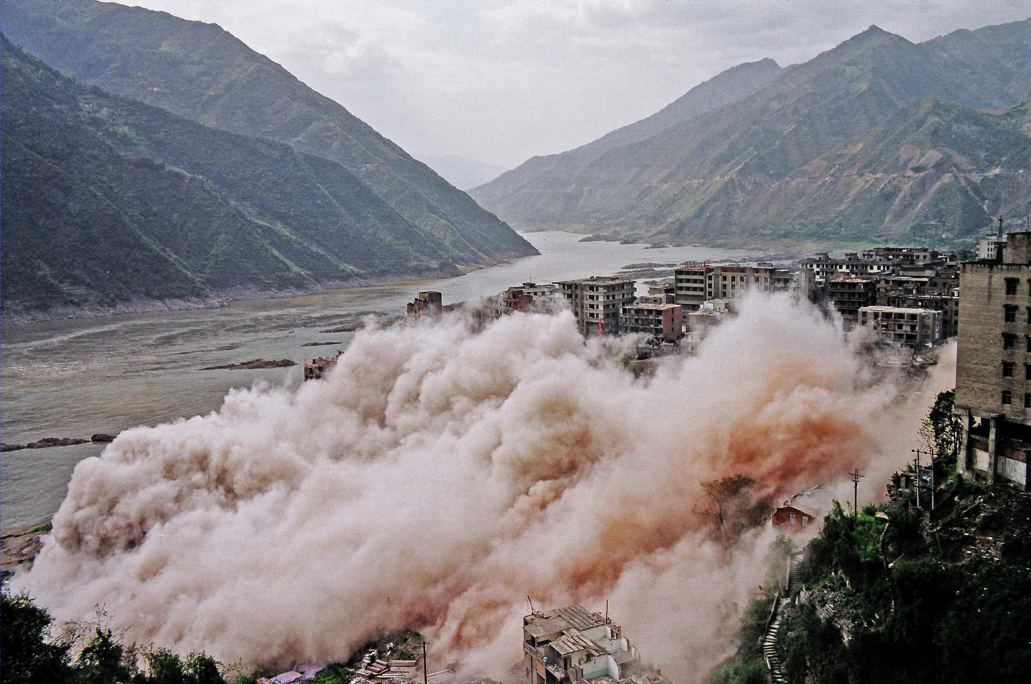 explosion in city along river with mountains in the background 